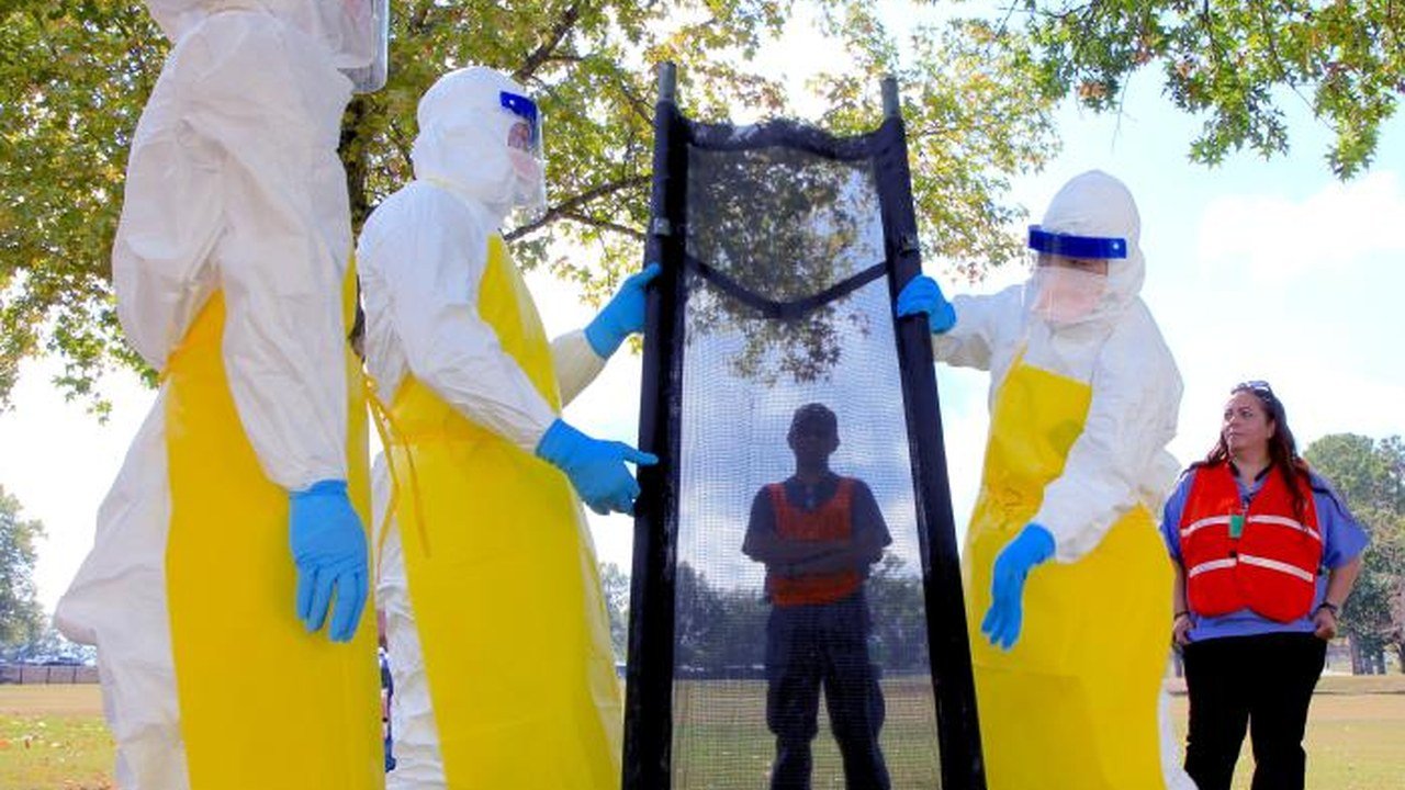 Healthcare workers in protective equipment disinfect a transport gurney during a 2014 Ebola response training exercise